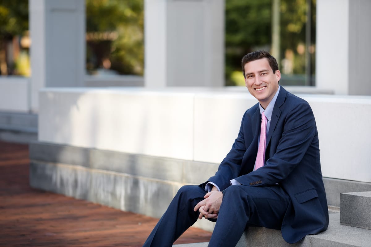 Logan Wease seated outdoors in a suit, smiling